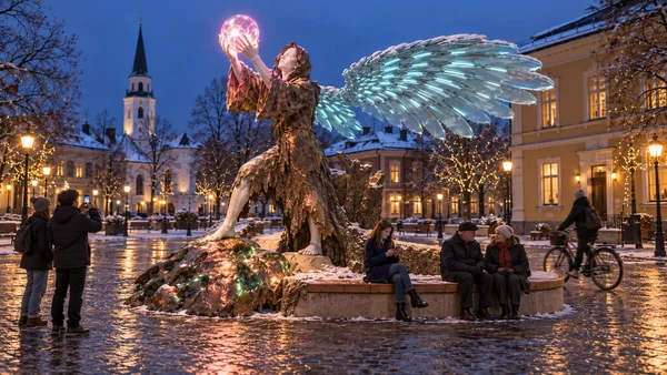 Wi-Fi Angel from the other side: the bronze lump with glowing cracks, the oak bench and a passing cyclist