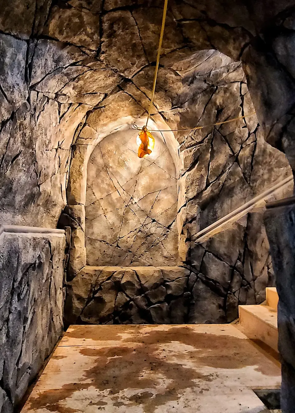 Cave-style stair landing with cracked rock walls, an arched niche and a single warm lamp