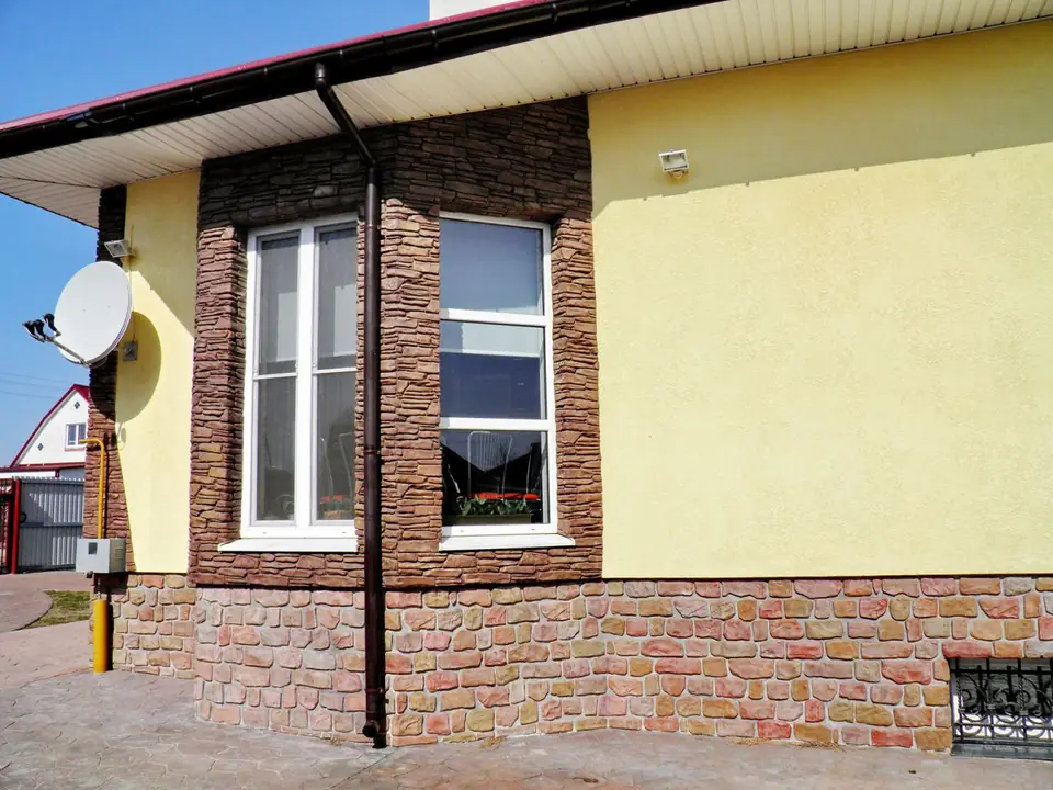 Corner window set in brown stone-effect cladding above a stone plinth
