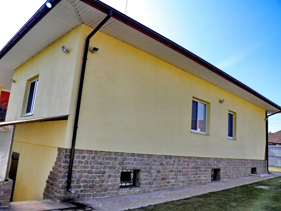 A yellow house with a stone-effect plinth in pink-brown tones