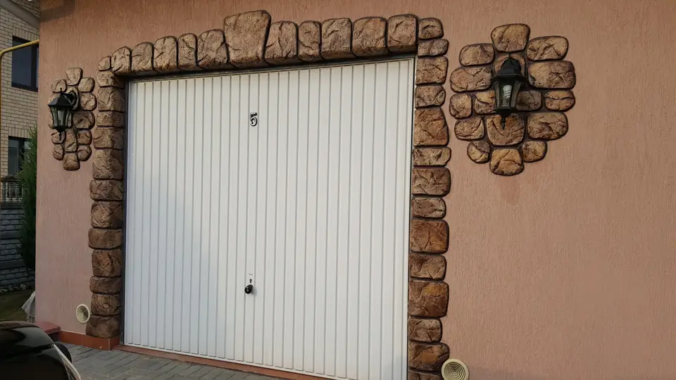Garage door framed by hand-modelled stone, with two wall lamps