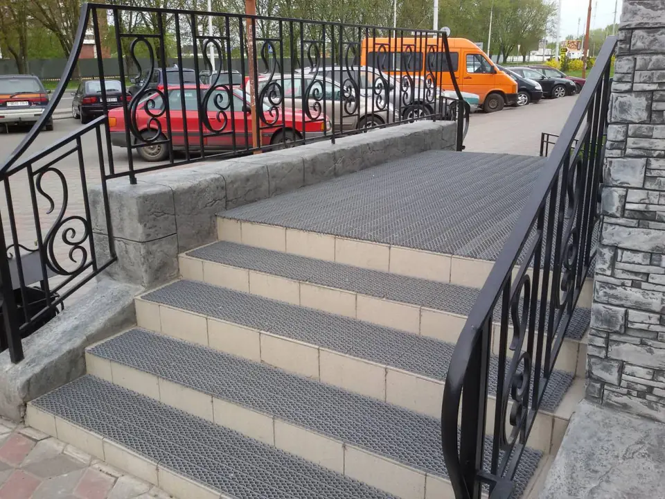 Entrance stairs with tiled treads between stone-clad walls and ironwork