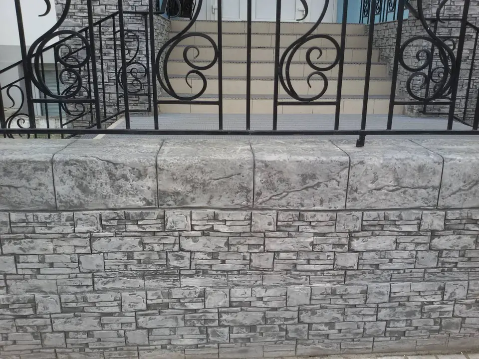 Close-up of a stone-effect wall under a wrought-iron railing