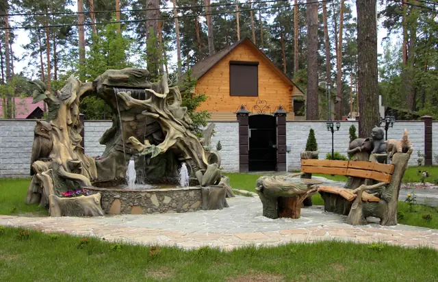 A garden fountain modelled as an old tree stump, with a log house behind