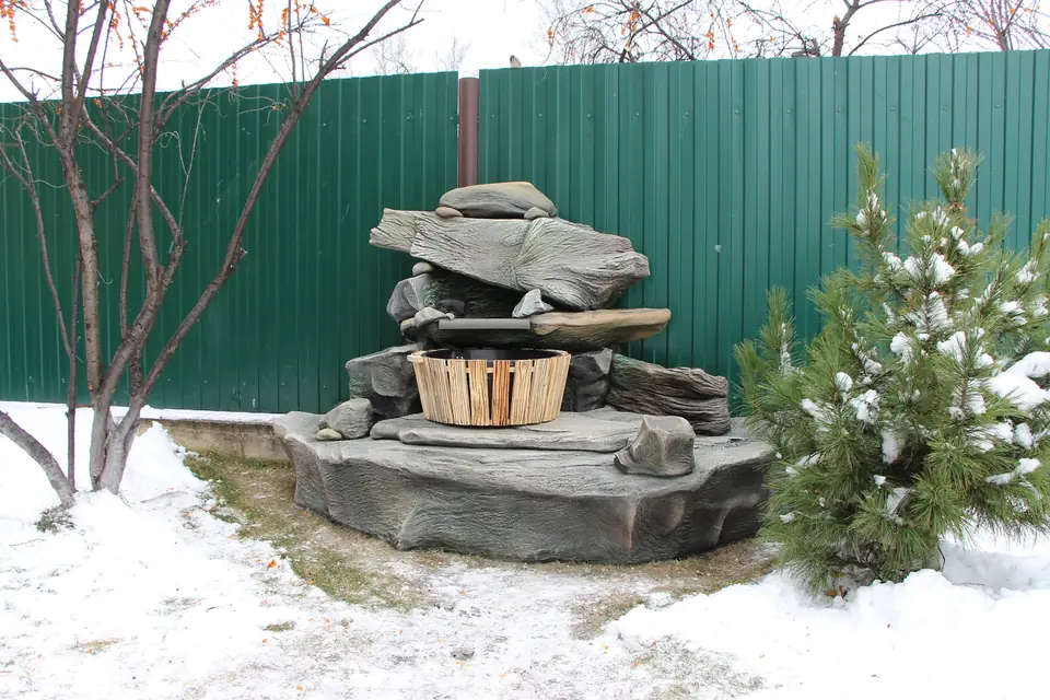 A fountain with a wooden barrel and driftwood-like rock slabs in winter