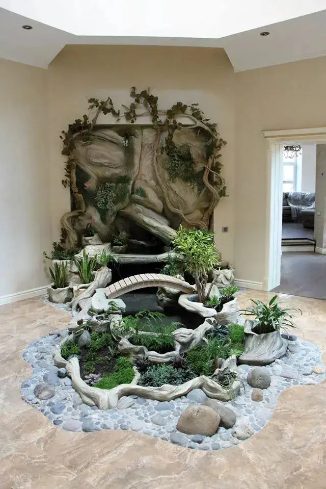 Indoor wall waterfall framed by carved trunk forms and plants