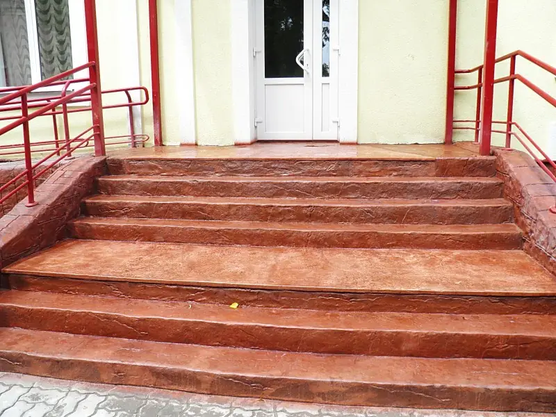 Entrance steps and landing in textured red-brown concrete under the door