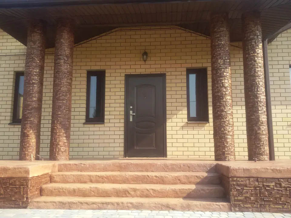 Entrance of a yellow brick house with tree-trunk columns and red-brown steps