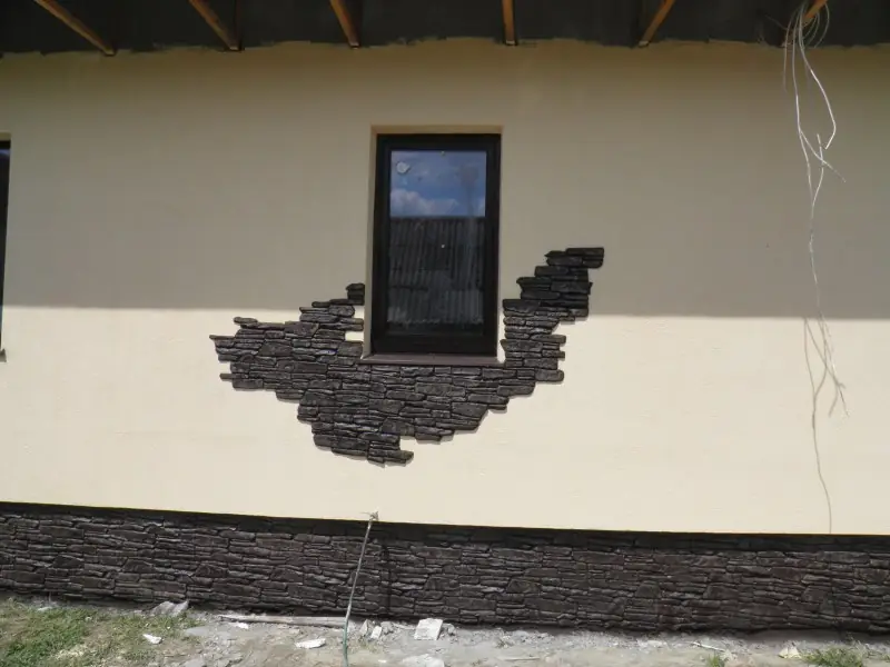 Window framed by irregular stone on a cream facade, with a dark stone plinth