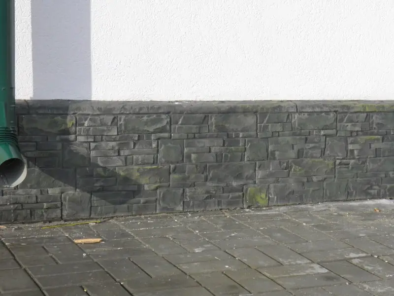 Dark stacked-stone plinth under a white wall, with a green downpipe