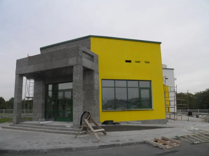 The entrance portal clad in dark stacked stone, against the yellow and grey facade