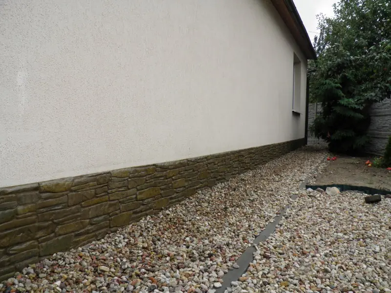 Long side wall with a dark stone plinth above a gravel path