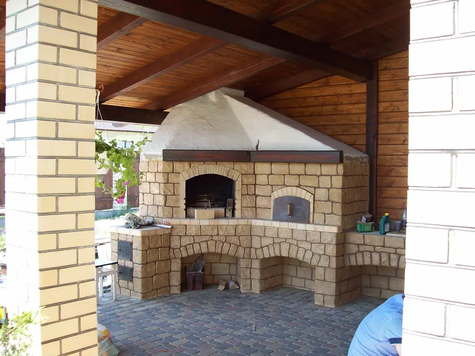 Brick-and-stone oven with a metal hood under a pitched wooden roof