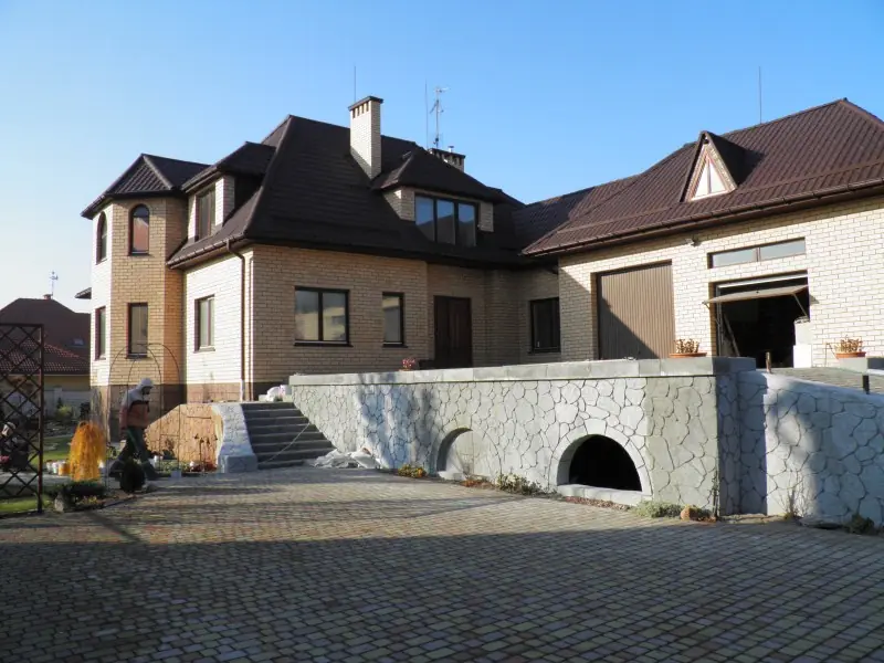 Driveway entrance flanked by arched, stone-faced retaining walls