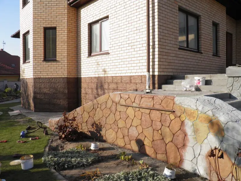 Low stone retaining wall beside the corner of a house, with steps