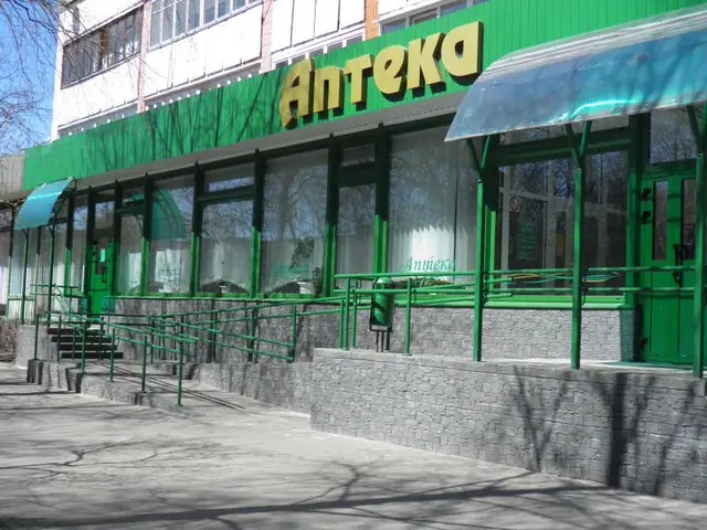 A pharmacy shopfront with a grey stone-effect plinth below the green frontage
