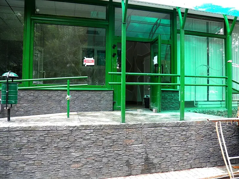 Layered dark-grey stone plinth below glazed pharmacy windows and green railings