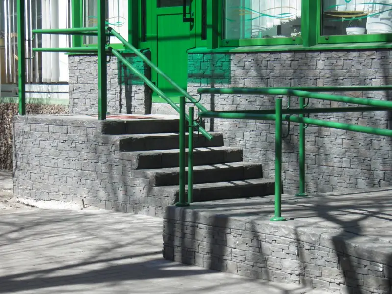 Entrance steps with green railings between stone-faced walls