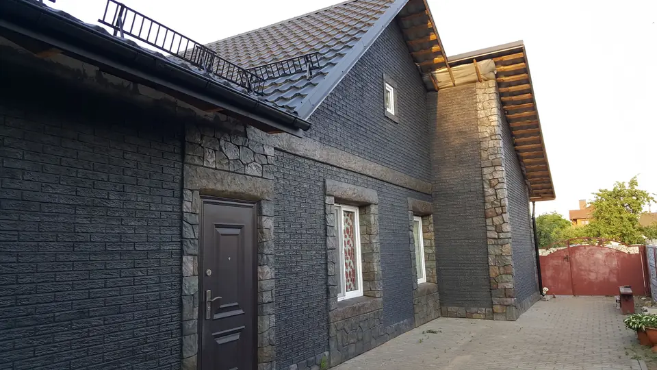Dark brick-effect house with stone window frames, beside the stone fence