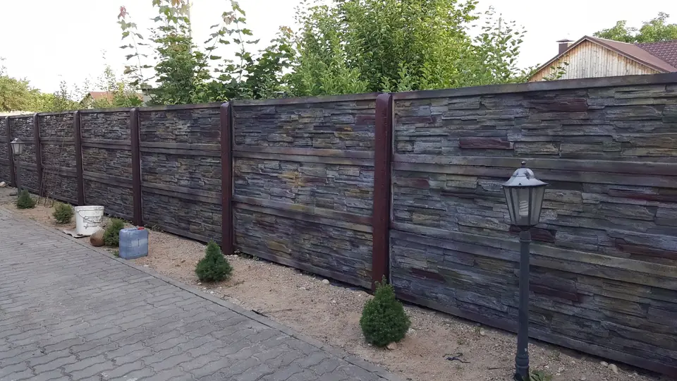 A long fence of stacked-stone panels in violet-grey and brown tones