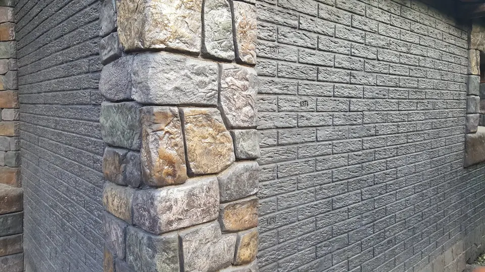 Rough stone quoins at the corner of a dark brick-effect wall