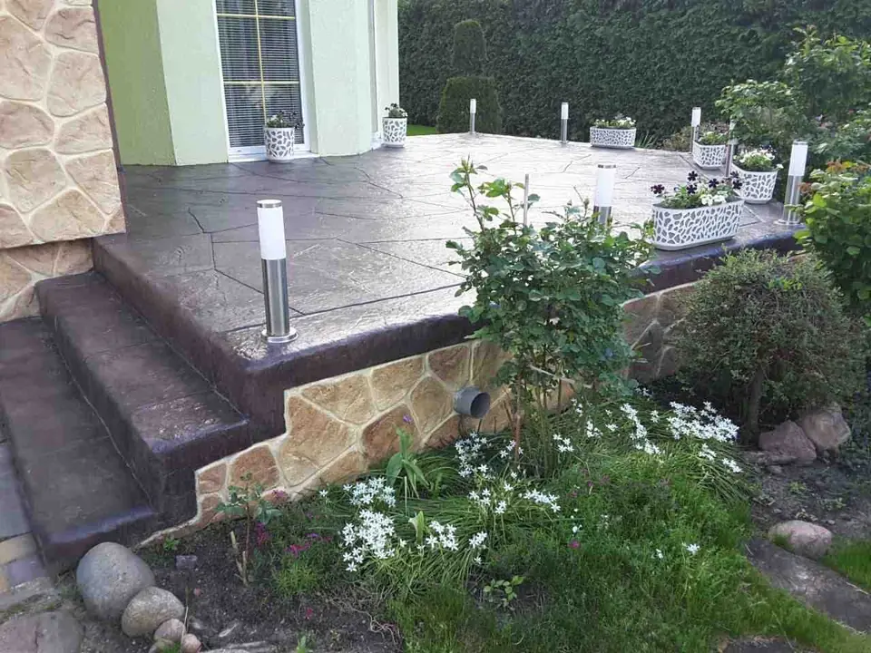 Terrace steps in stamped concrete beside a stone retaining wall and garden