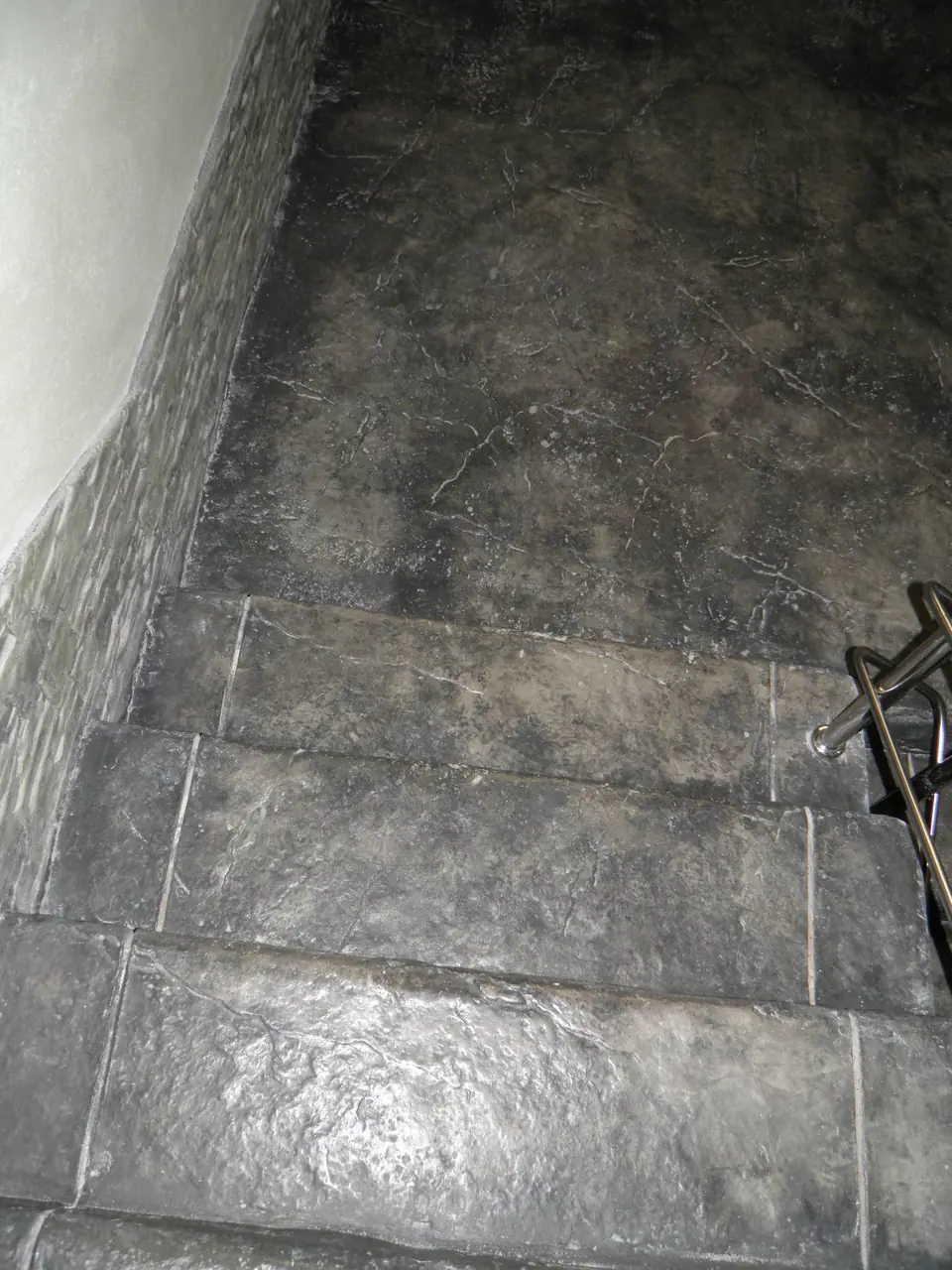 Sisetrepid ja põrand templitud betoonis, viimistletud tumeda plaatkivina, kõrval kaldkivist seinakate