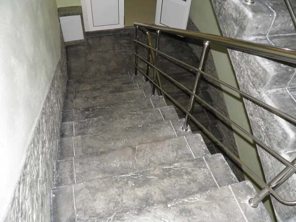 Interior stair in grey stone-textured concrete with a stainless handrail and stone cladding along the wall