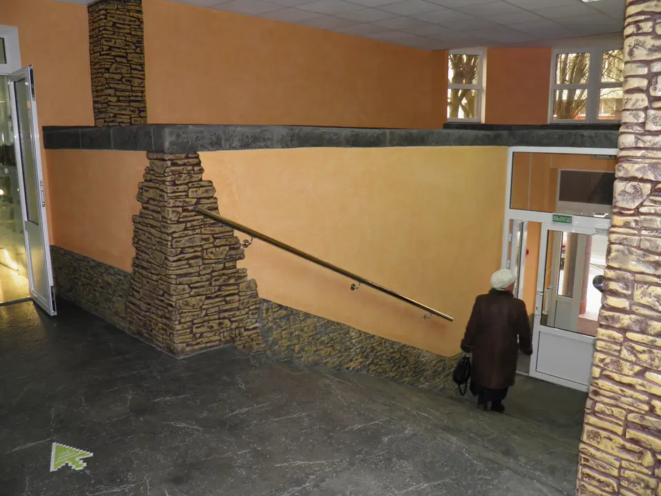 Entrance hall with a rough stone-clad wall edge against orange plaster and a stone-textured floor