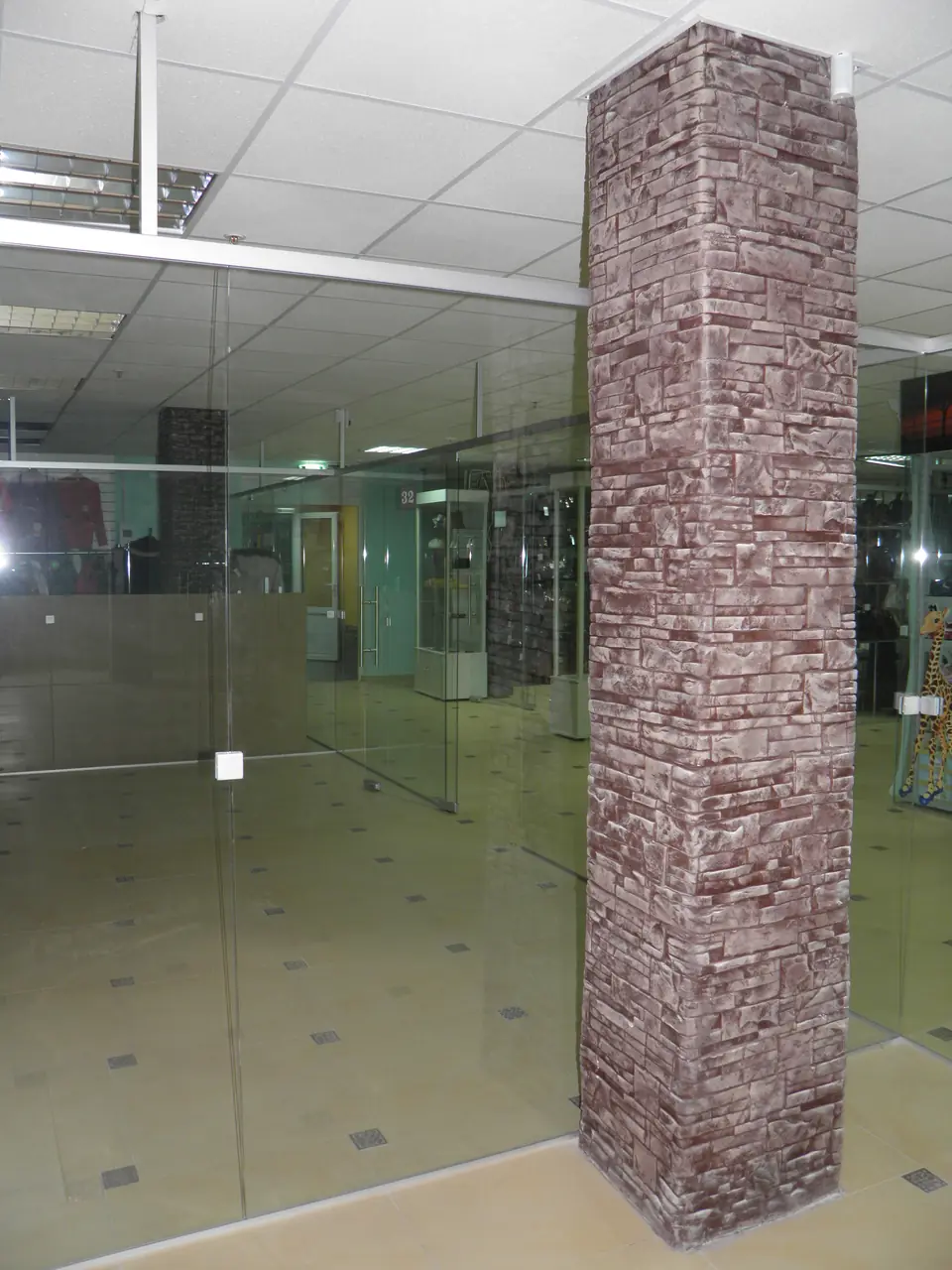 A square column clad in stone-effect panels in a glazed hall