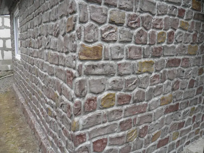 Corner of a rubble-stone wall: rounded stones in grey, rust and violet