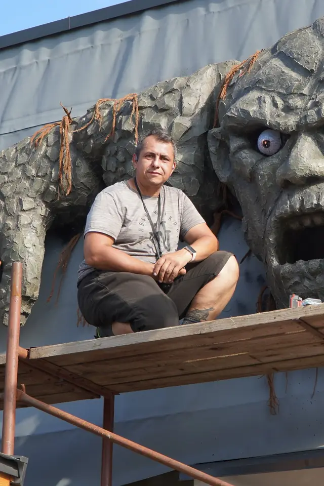 Aleks Svirydzenka sitting on a working platform in front of the sculpted stone face of the guardian during installation