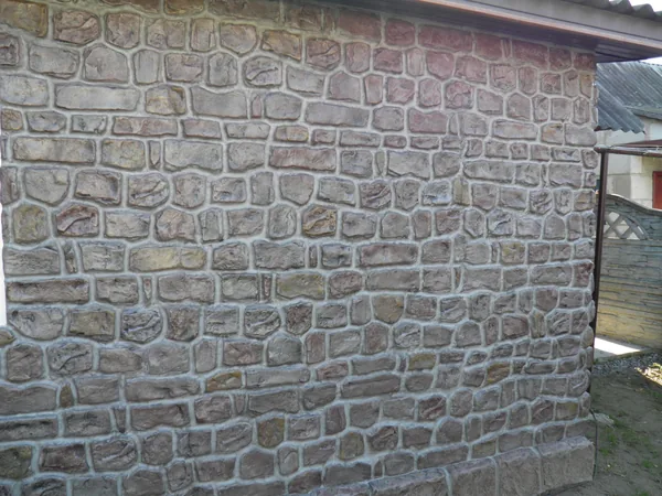 Long wall under the eaves: stones in grey, rust, ochre and violet