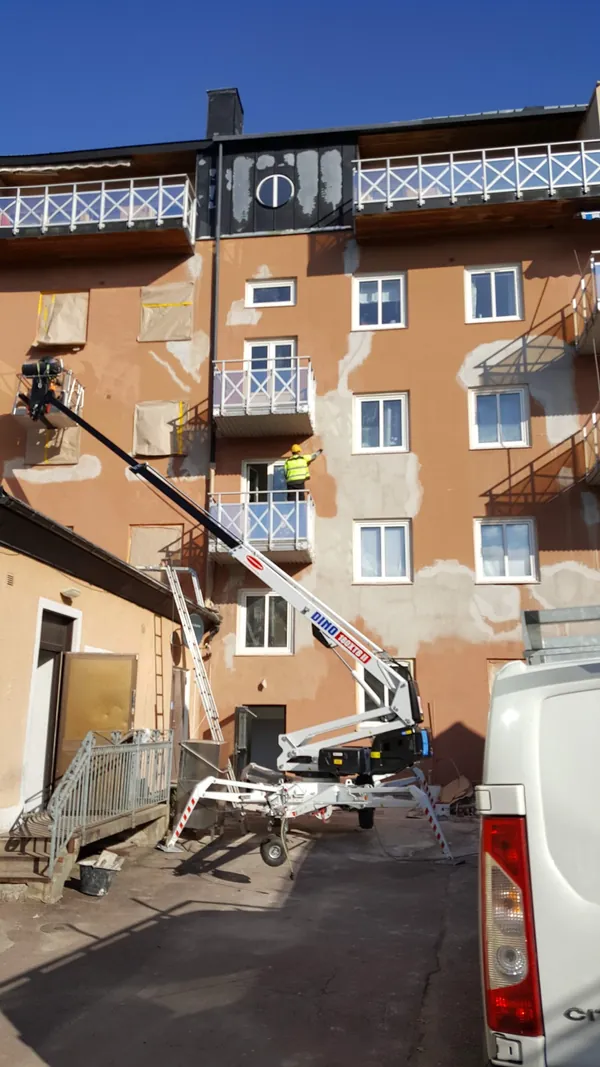 Reparación del revoco desde una plataforma elevadora: enlucido nuevo trabajado sobre la superficie antigua alrededor de las ventanas