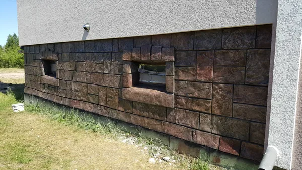 Long plinth wall with two window surrounds in warm red-brown tones