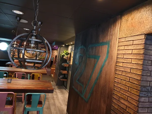 الجدار بمظهر خشبي بالرقم 27 بجانب عمود من الطوب محفور عليه “The Pub 27”