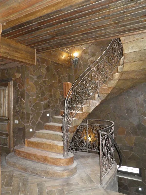 The finished spiral staircase: stone-look treads under a forged railing with oak leaves