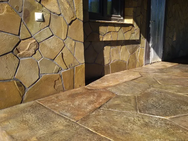 The terrace floor in sunlight: flagstones in honey and rust tones along the stone-clad wall