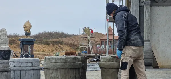 Modelling timber-look barrels in fresh mortar on site, with the Viking ship and a mascot on its pedestal behind