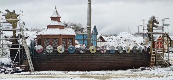 The Viking ship under snow: hull, shields and the dragon prow and stern on scaffolding, work continuing through the winter