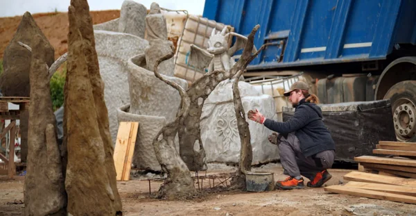 Hand-modelling a twisted tree trunk in fresh mortar, with a small dragon sculpture waiting behind